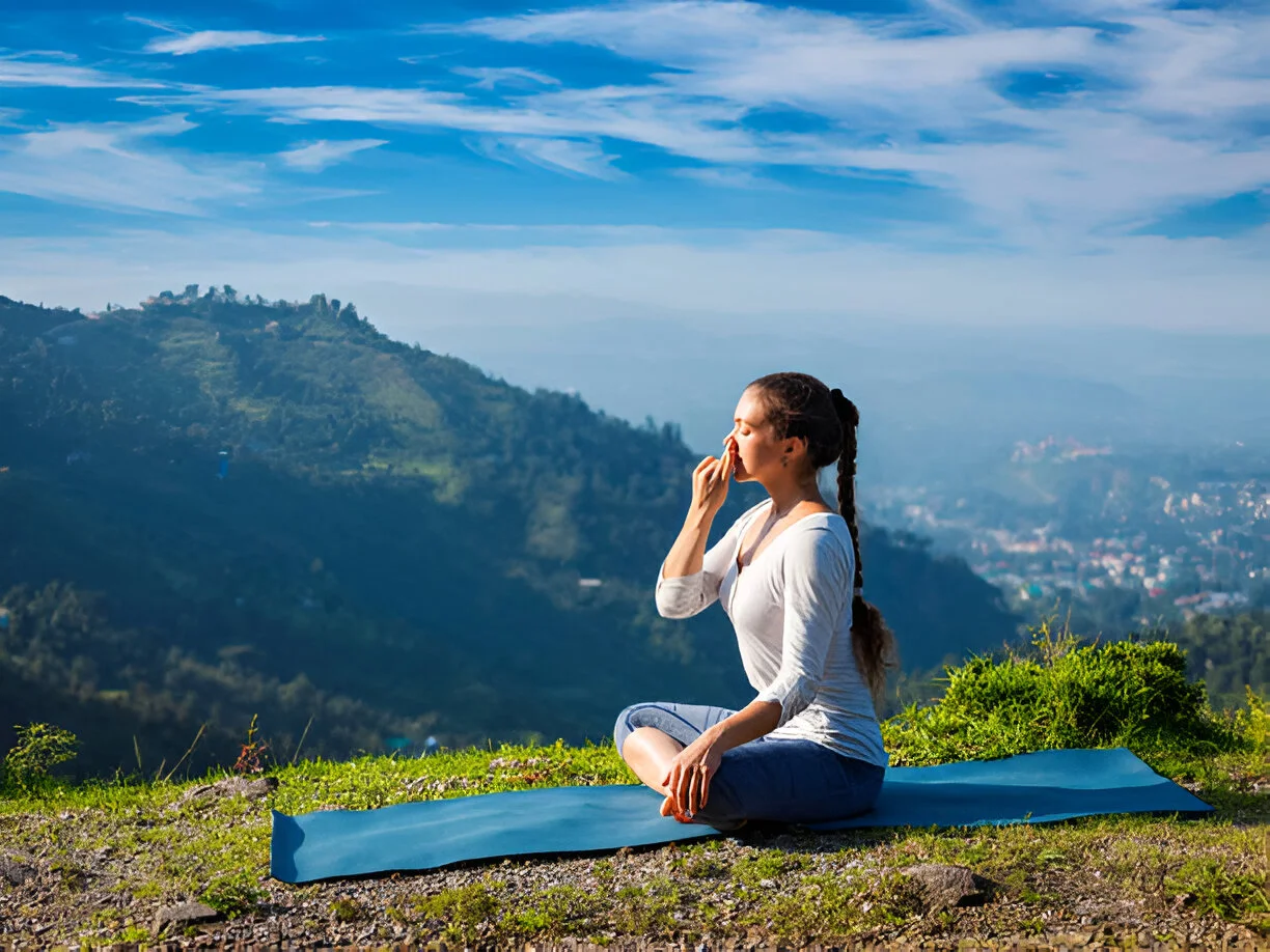 A woman breathing through one nostril on a mountainside